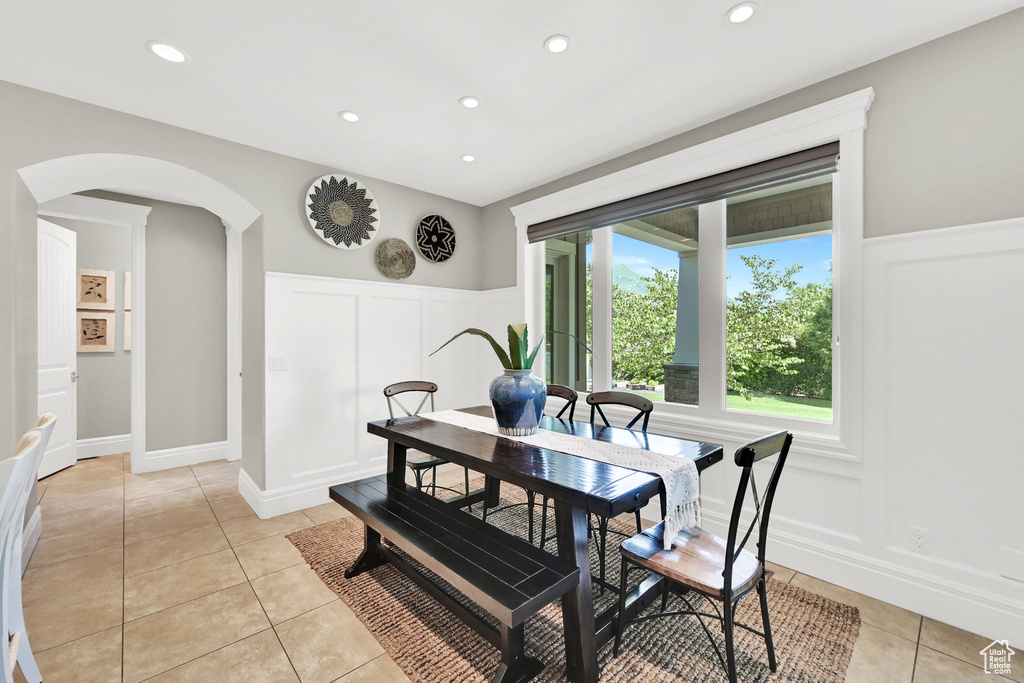 Dining space featuring arched walkways, light tile patterned flooring, a decorative wall, a wainscoted wall, and recessed lighting
