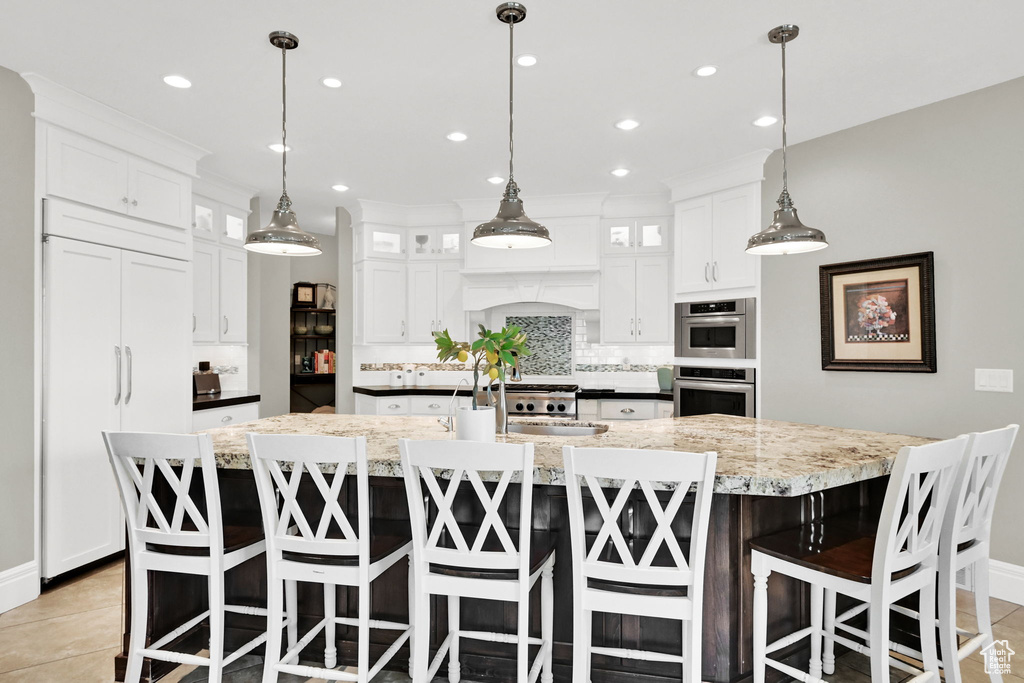 Kitchen with paneled refrigerator, backsplash, a large island, white cabinets, and light tile patterned flooring