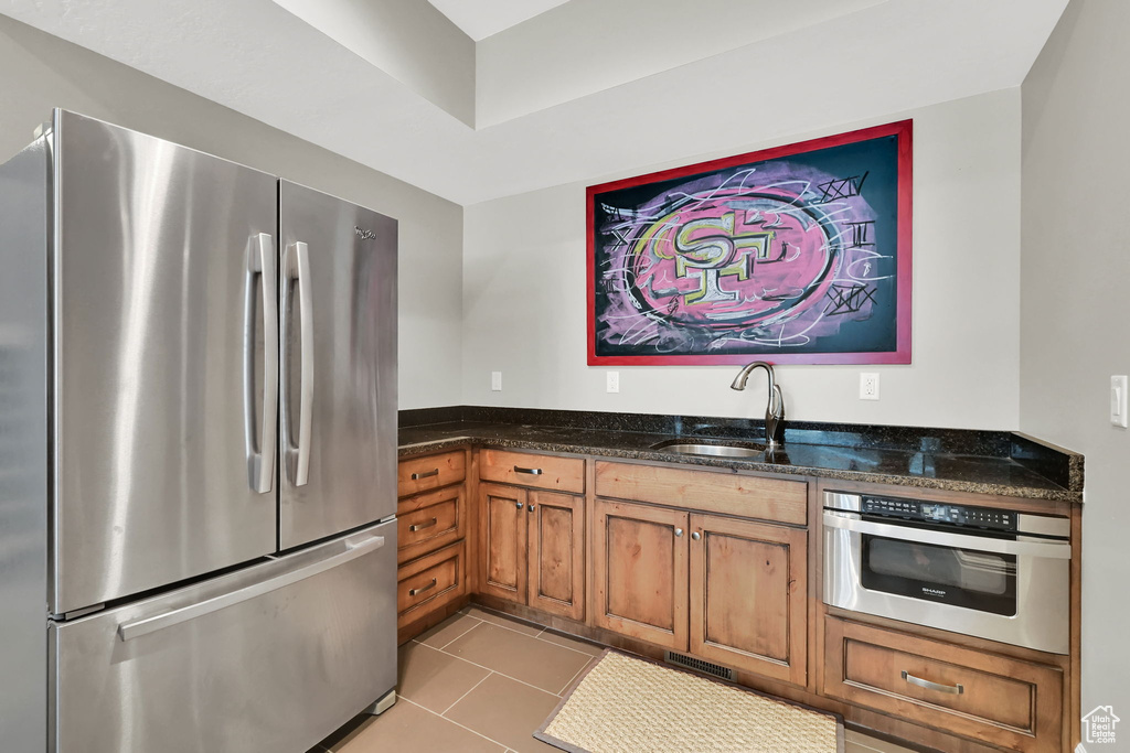 Kitchen featuring freestanding refrigerator, oven, a sink, brown cabinets, and dark stone countertops