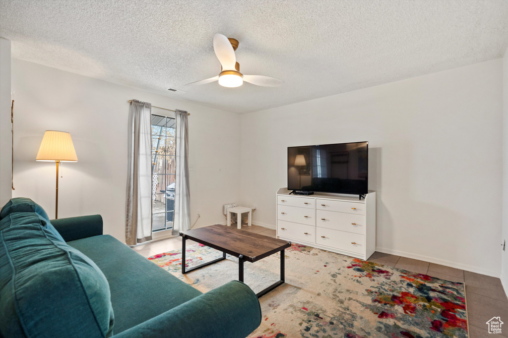 Living room with a ceiling fan, a textured ceiling, tile patterned flooring, and baseboards