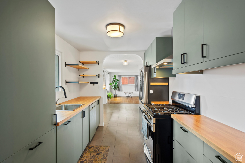 Kitchen with appliances with stainless steel finishes, a sink, wooden counters, arched walkways, and wall chimney exhaust hood