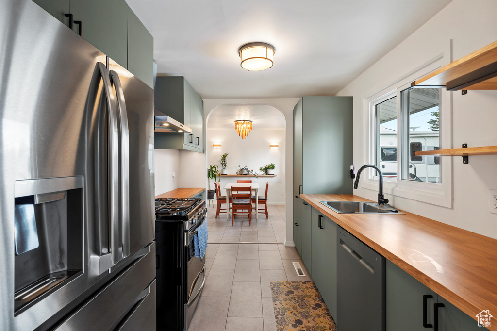 Kitchen with stainless steel appliances, a sink, butcher block counters, arched walkways, and green cabinetry