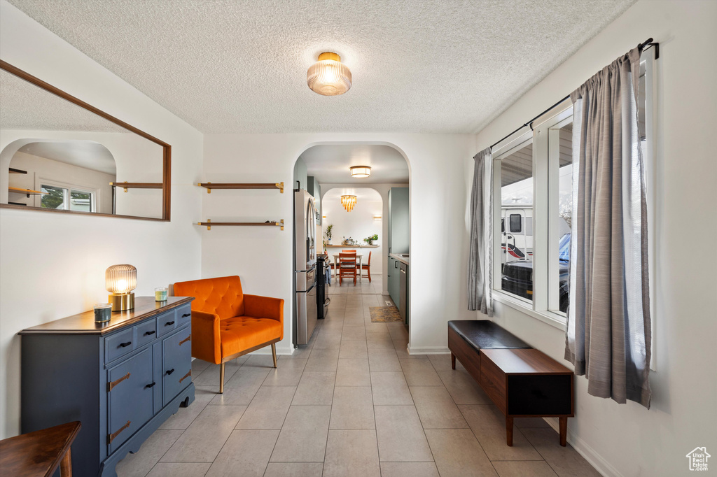 Corridor featuring arched walkways, a textured ceiling, light tile patterned floors, and baseboards