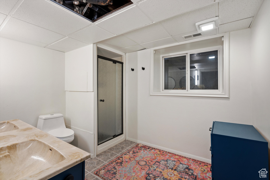 Bathroom with a paneled ceiling, toilet, a shower stall, and double vanity