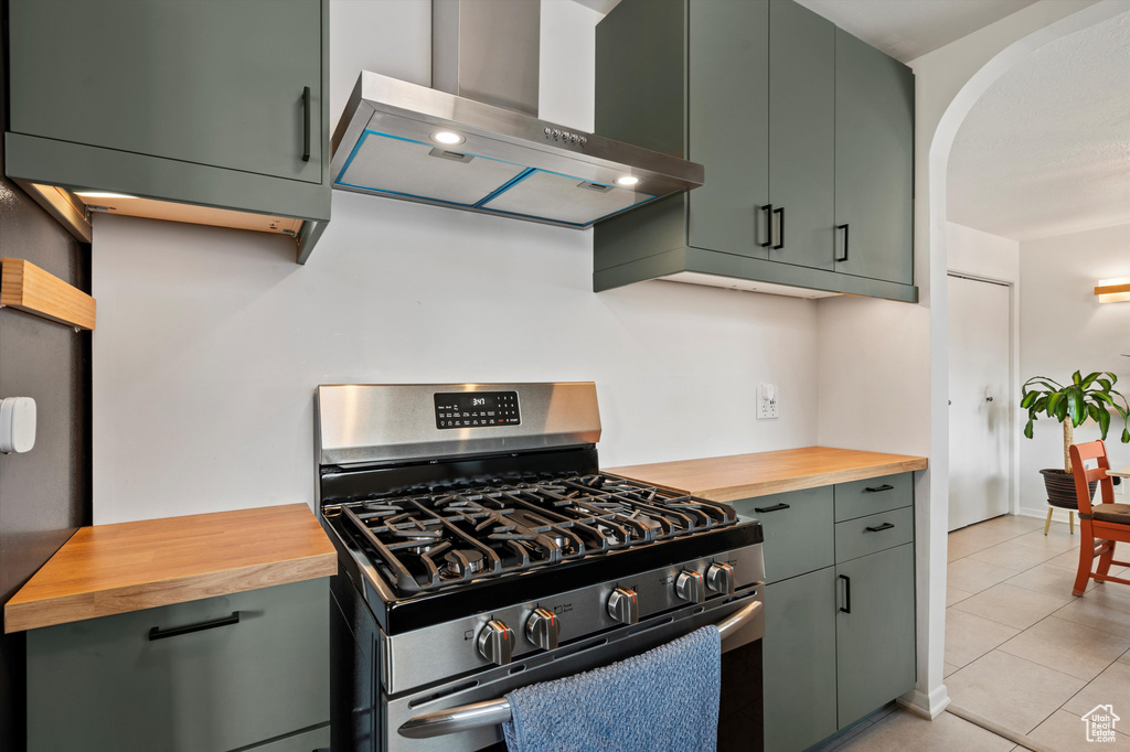 Kitchen with stainless steel gas range oven, wooden counters, wall chimney exhaust hood, light tile patterned floors, and arched walkways