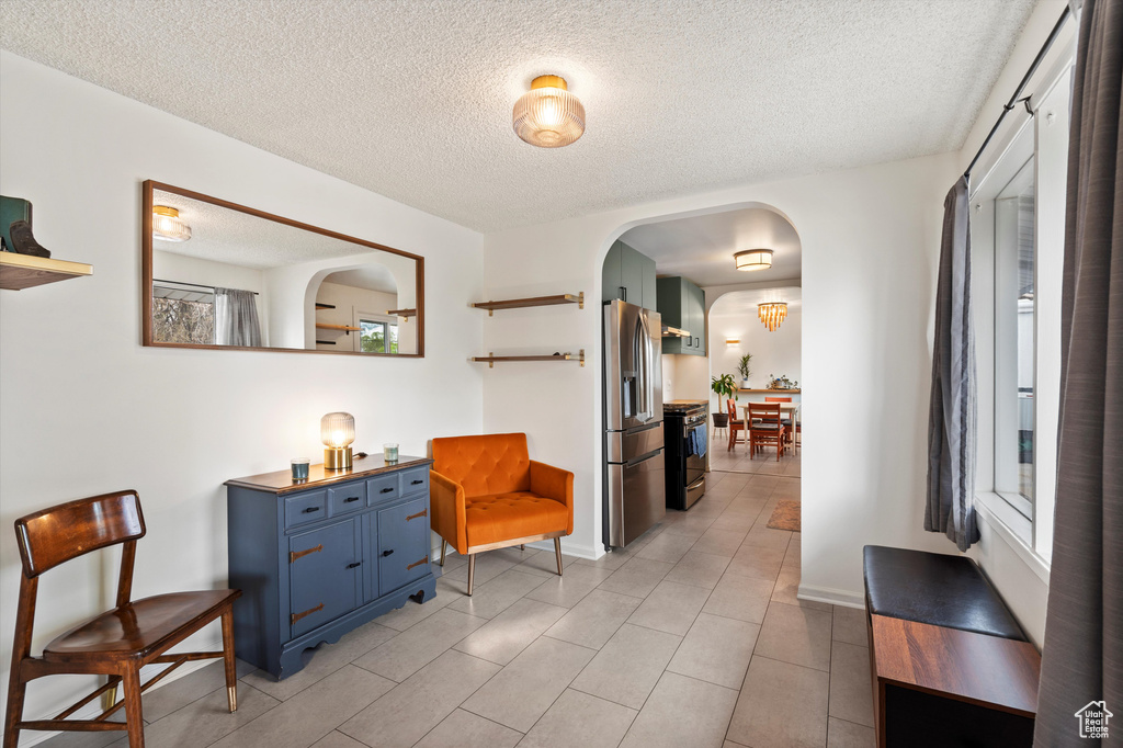 Hallway with arched walkways, a textured ceiling, light tile patterned floors, and baseboards