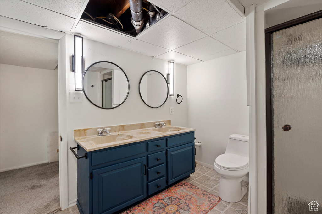 Bathroom with double vanity, toilet, baseboards, a paneled ceiling, and a shower with shower door