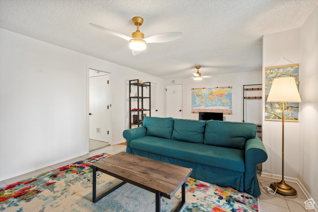 Living area featuring ceiling fan, light tile patterned floors, a textured ceiling, and baseboards