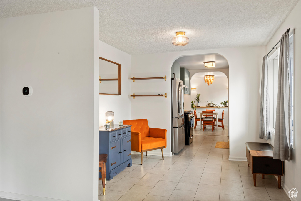 Corridor with arched walkways, a textured ceiling, baseboards, and light tile patterned floors