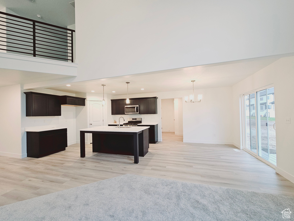 Kitchen with stainless steel microwave, a chandelier, an island with sink, light wood-style flooring, and recessed lighting
