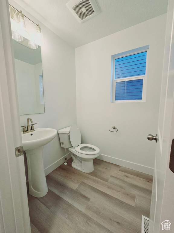 Half bathroom featuring toilet, wood finished floors, baseboards, and a sink