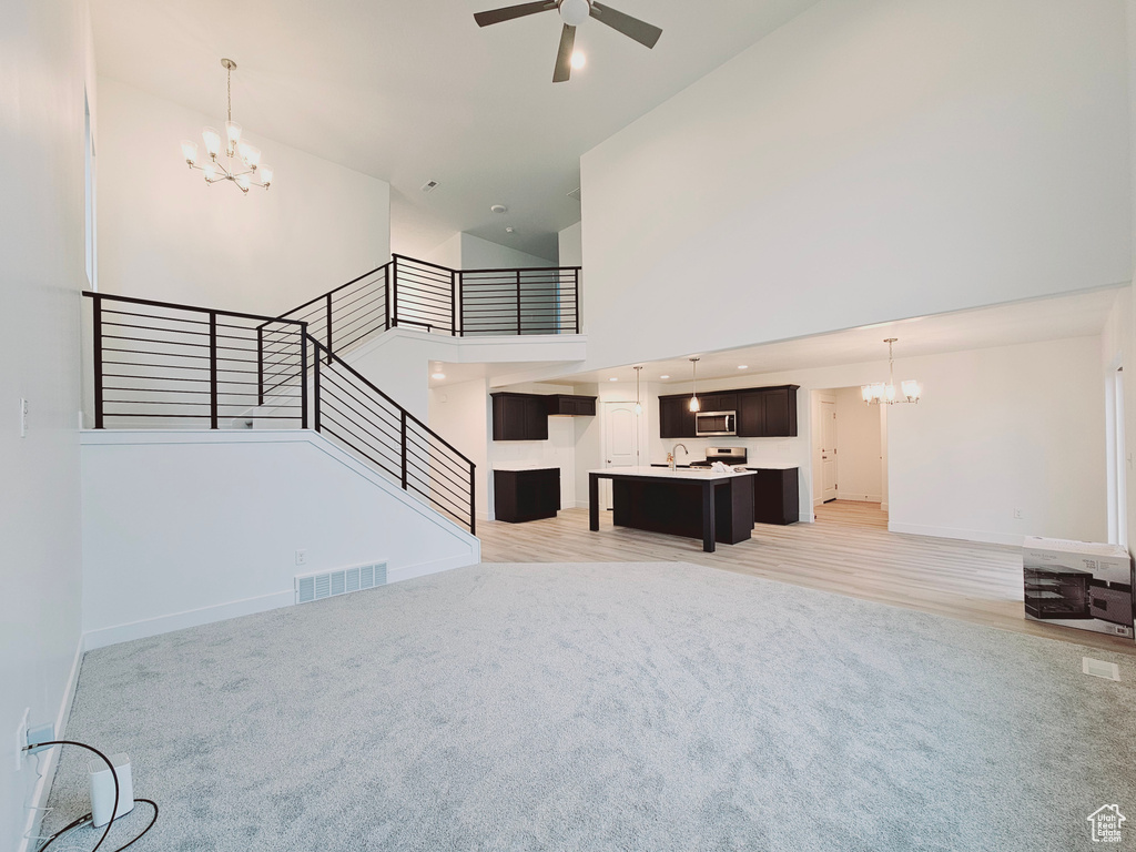 Unfurnished living room featuring a chandelier, high vaulted ceiling, light colored carpet, a ceiling fan, and stairway