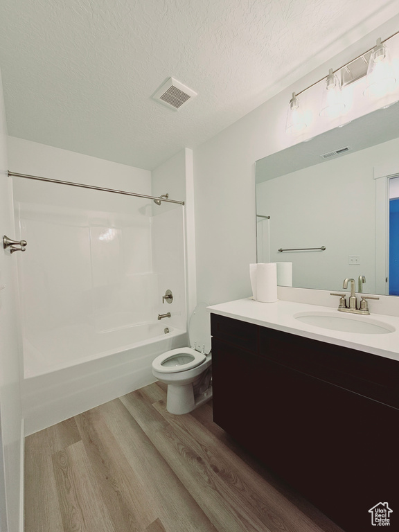 Full bath featuring wood finished floors, toilet, tub / shower combination, vanity, and a textured ceiling