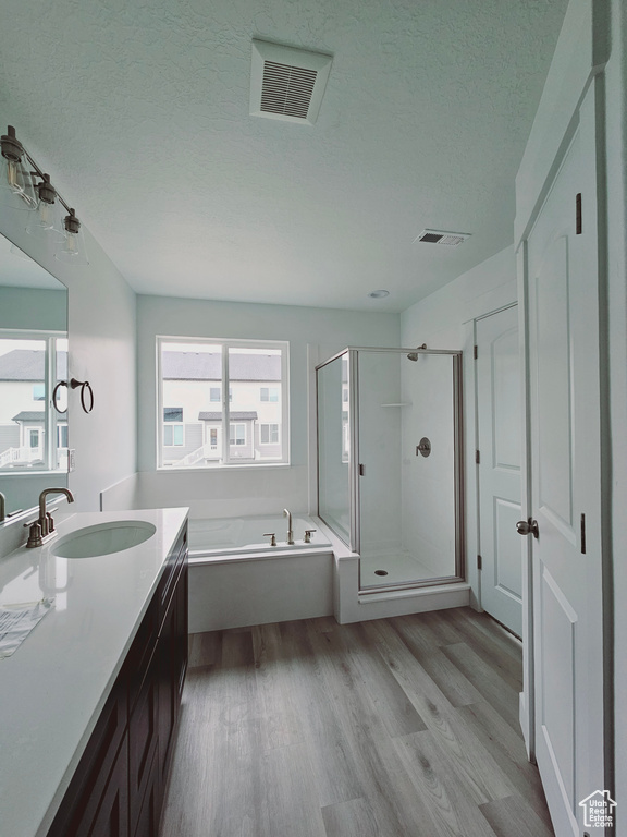 Bathroom with wood finished floors, vanity, a stall shower, a bath, and a textured ceiling