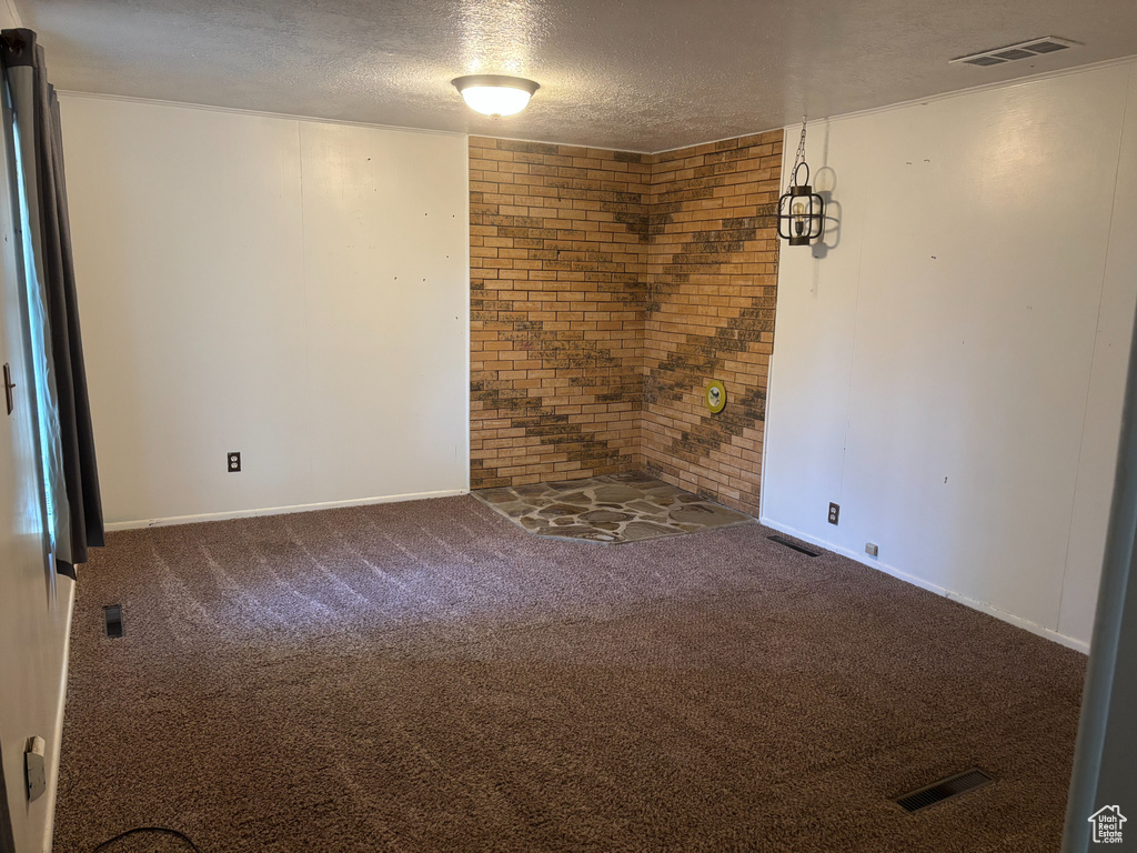 Carpeted empty room featuring a textured ceiling, brick wall, and baseboards