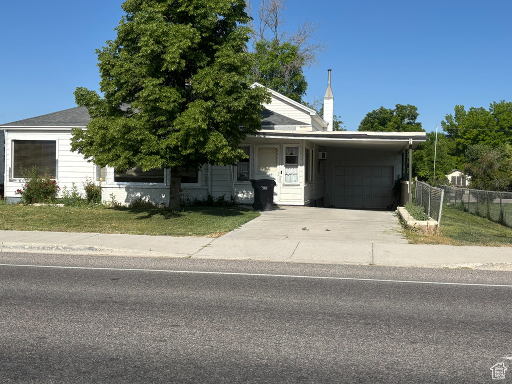 View of property hidden behind natural elements with a carport, concrete driveway, a chimney, and a garage