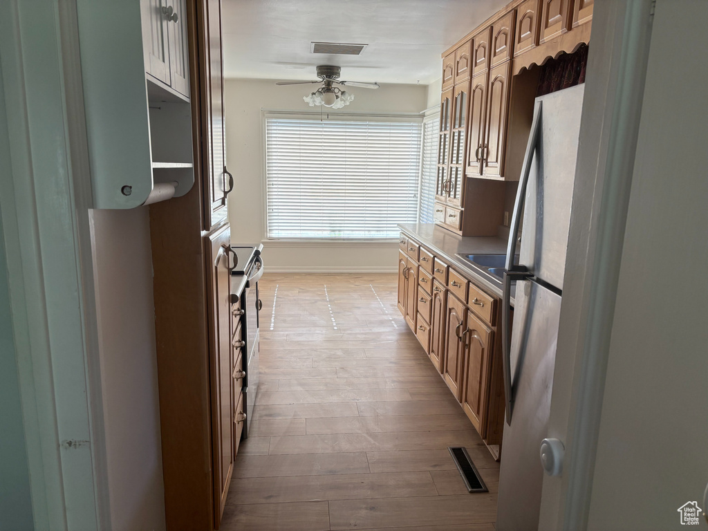Kitchen featuring light wood finished floors, ceiling fan, stainless steel appliances, and baseboards