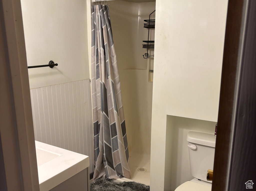 Full bath with toilet, wood finished floors, a stall shower, vanity, and a wainscoted wall