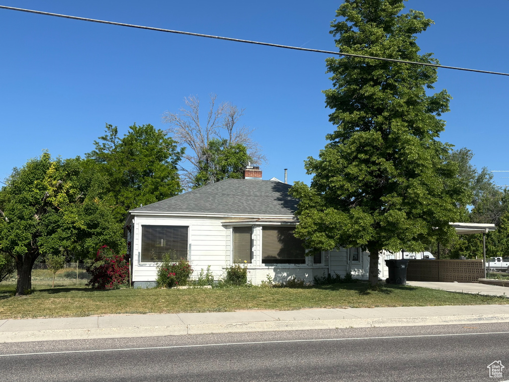 View of property hidden behind natural elements featuring a chimney and a shingled roof