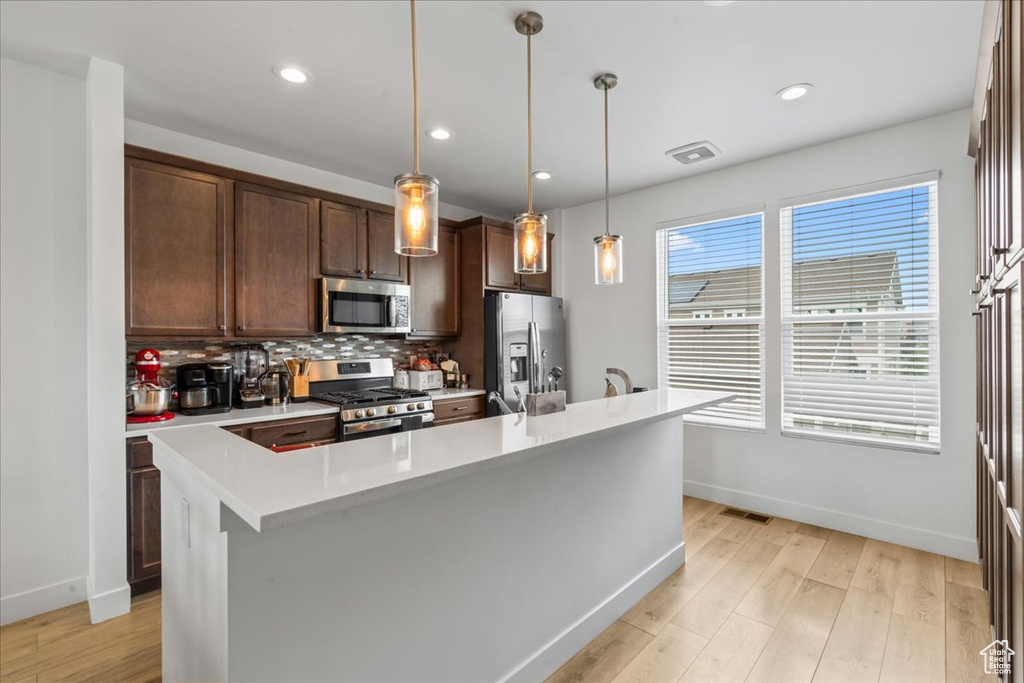 Kitchen featuring appliances with stainless steel finishes, baseboards, light countertops, decorative backsplash, and light wood-type flooring