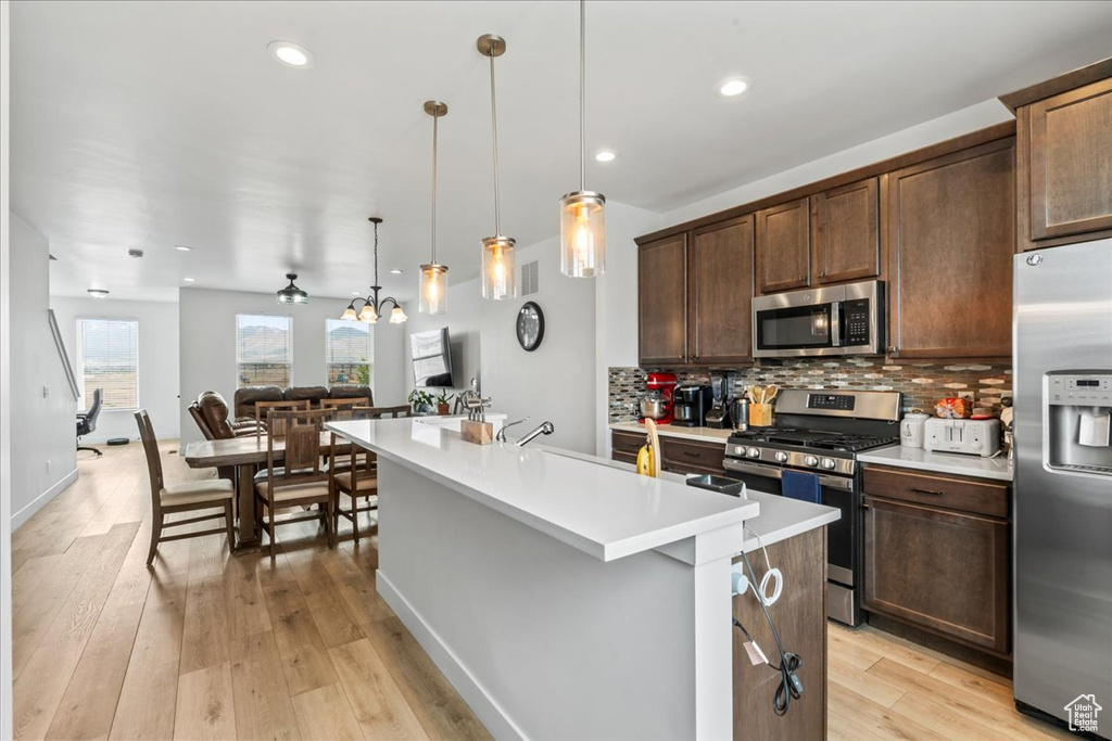Kitchen with stainless steel appliances, a center island with sink, light countertops, decorative backsplash, and dark brown cabinetry