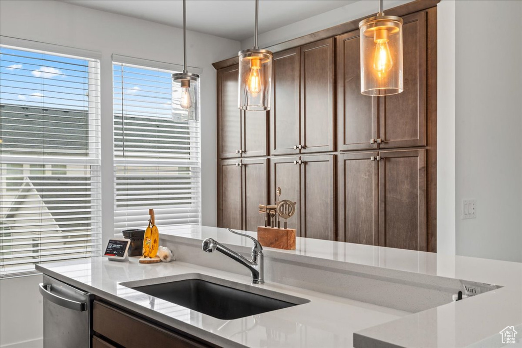 Kitchen featuring a sink, stainless steel dishwasher, hanging light fixtures, and light stone countertops
