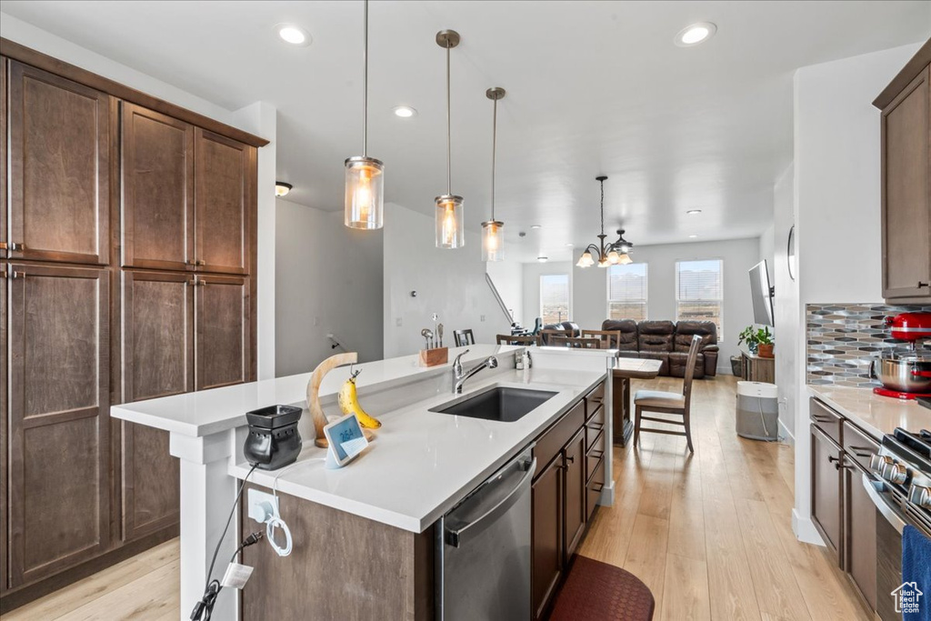Kitchen featuring stainless steel appliances, a sink, light wood finished floors, a kitchen island with sink, and light countertops