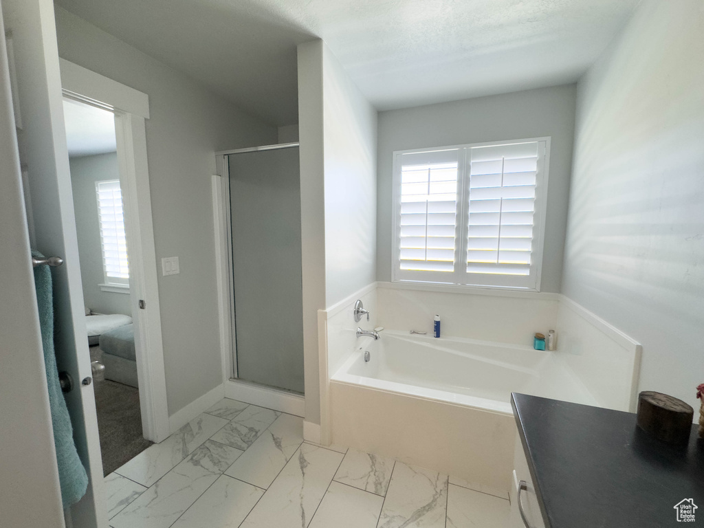 Bathroom with a garden tub, a shower stall, marble look tile flooring, and vanity