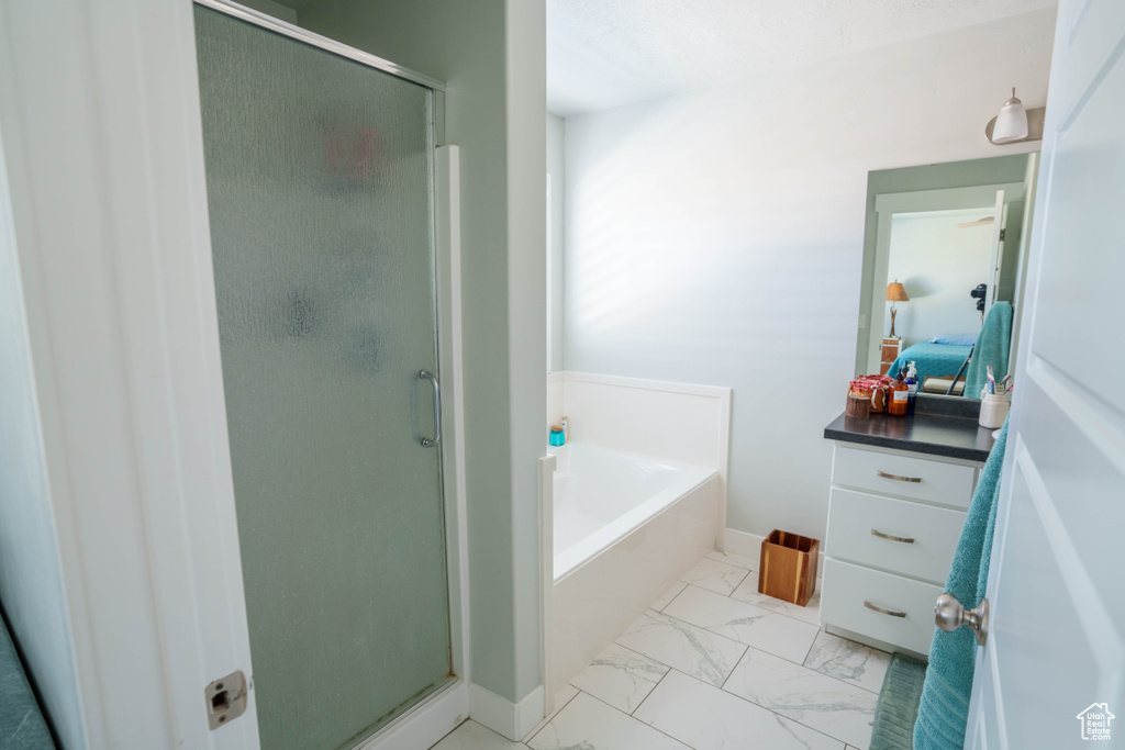 Full bathroom featuring a stall shower, a garden tub, marble look tiles, ensuite bath, and baseboards