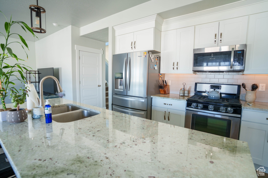 Kitchen with stainless steel appliances, a sink, decorative backsplash, white cabinetry, and light stone countertops