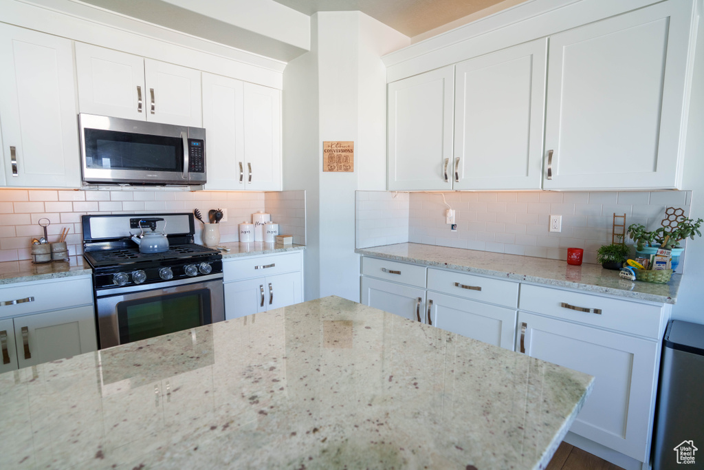 Kitchen featuring appliances with stainless steel finishes, white cabinets, light stone countertops, and backsplash