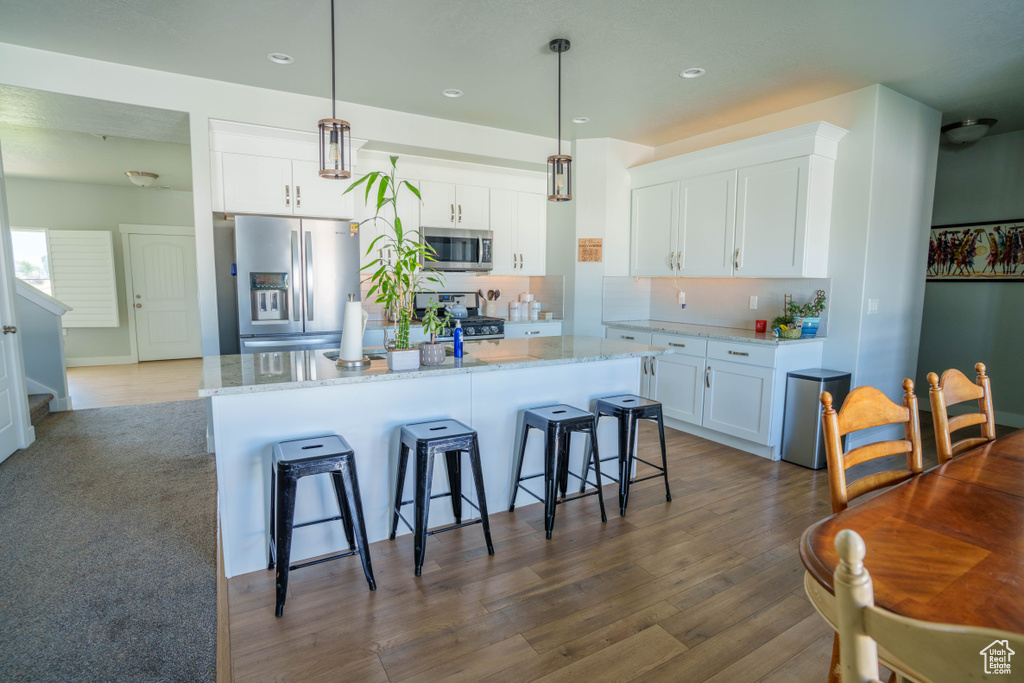 Kitchen with appliances with stainless steel finishes, recessed lighting, white cabinets, tasteful backsplash, and a center island with sink