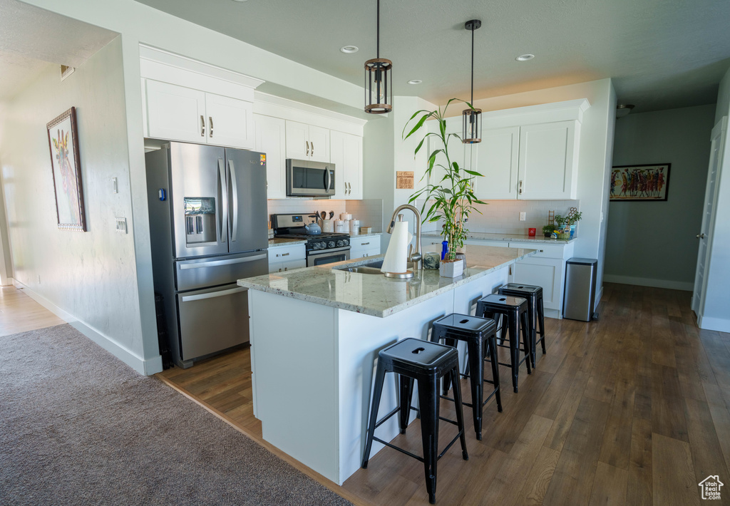 Kitchen with appliances with stainless steel finishes, baseboards, a kitchen breakfast bar, light stone counters, and white cabinetry