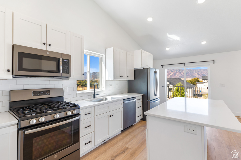 Kitchen with stainless steel appliances, a kitchen island, lofted ceiling, backsplash, and light countertops