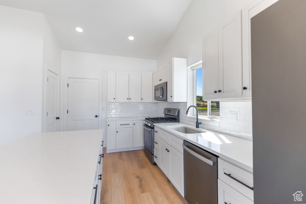 Kitchen with appliances with stainless steel finishes, a sink, backsplash, light wood finished floors, and white cabinets