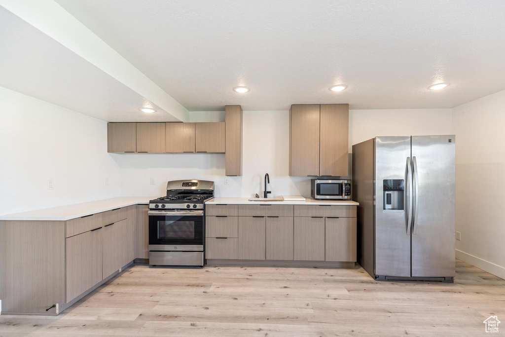 Kitchen featuring stainless steel appliances, light wood-style flooring, recessed lighting, light countertops, and a sink