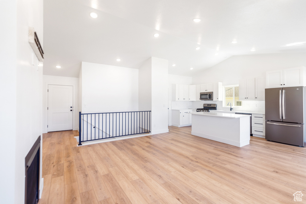 Kitchen with appliances with stainless steel finishes, a kitchen island, white cabinetry, a sink, and vaulted ceiling