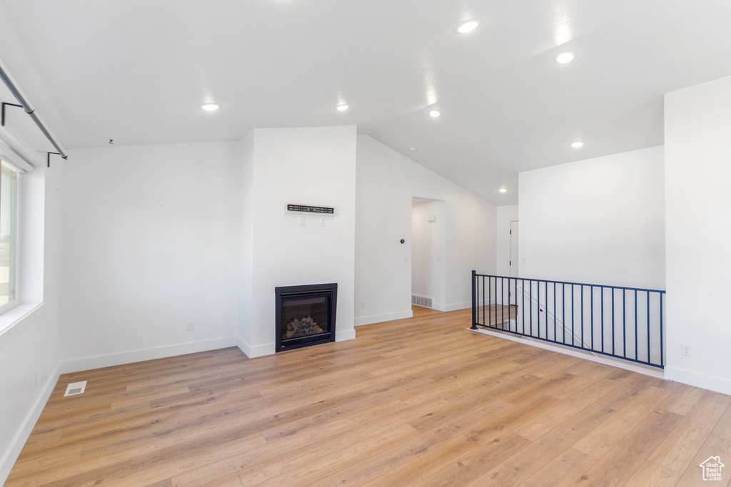Unfurnished living room with light wood-style floors, recessed lighting, baseboards, a glass covered fireplace, and vaulted ceiling