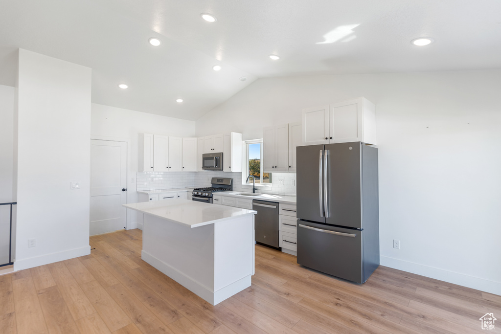 Kitchen with appliances with stainless steel finishes, white cabinetry, a kitchen island, light countertops, and decorative backsplash