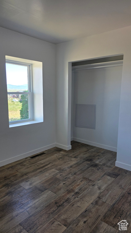 Unfurnished bedroom featuring dark wood-type flooring, a closet, and baseboards