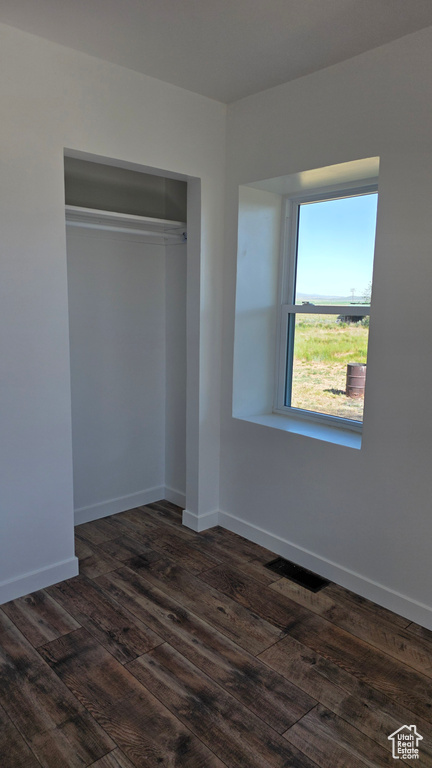 Unfurnished bedroom featuring dark wood-style flooring, baseboards, and a closet