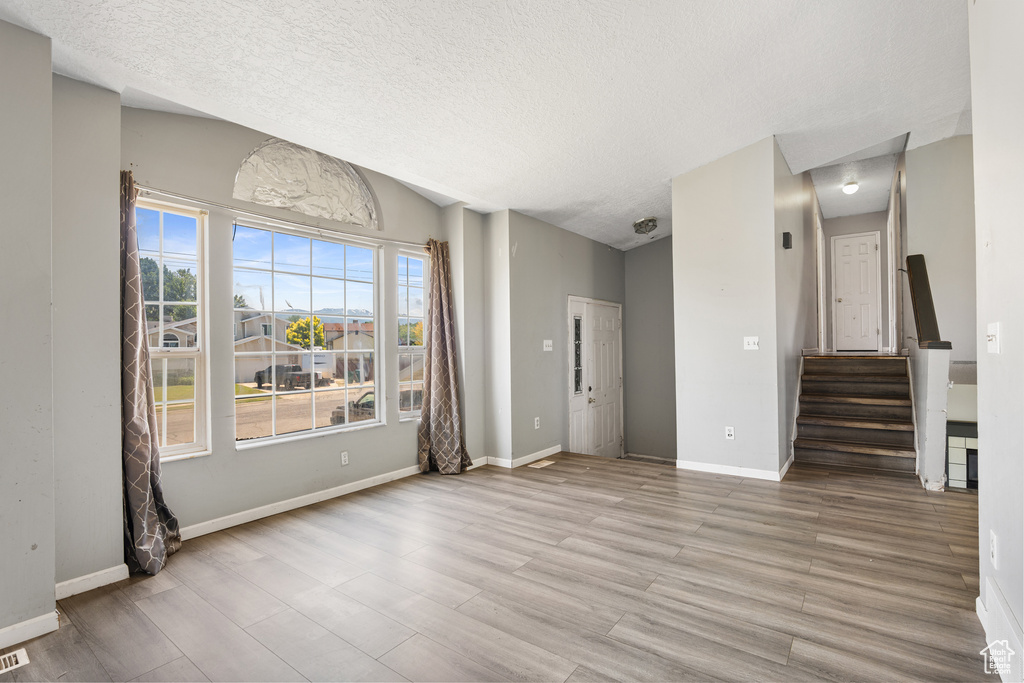 Unfurnished living room featuring a textured ceiling, light wood-style flooring, stairs, baseboards, and lofted ceiling