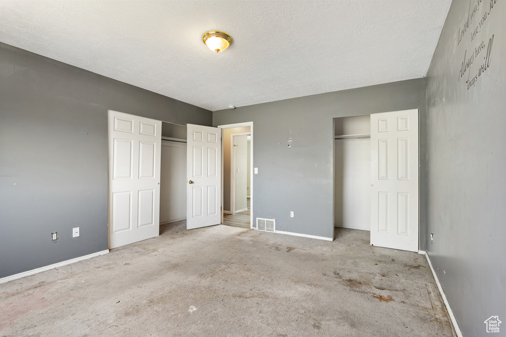 Unfurnished bedroom featuring two closets, baseboards, carpet floors, and a textured ceiling