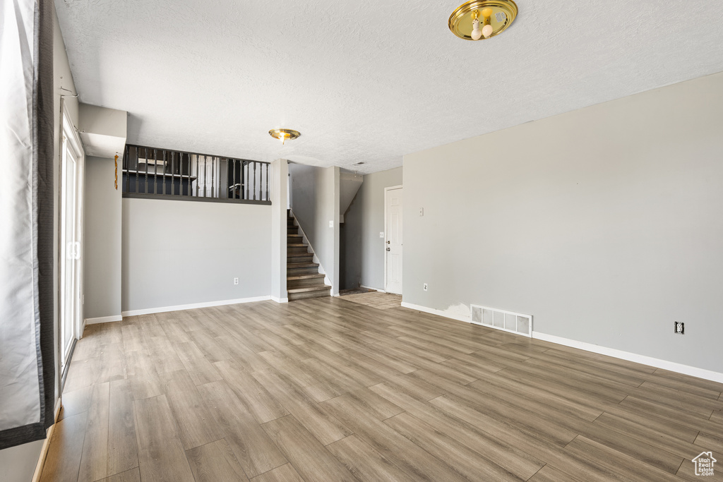 Unfurnished living room featuring wood finished floors, stairway, a textured ceiling, and baseboards