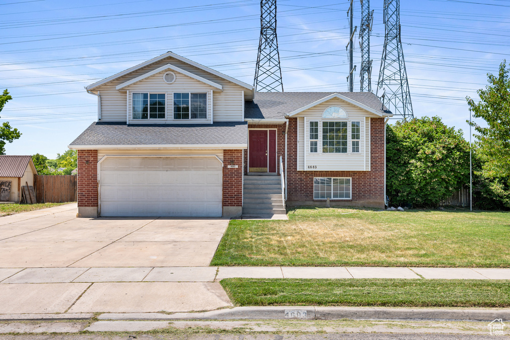 Tri-level home with an attached garage, brick siding, driveway, and roof with shingles