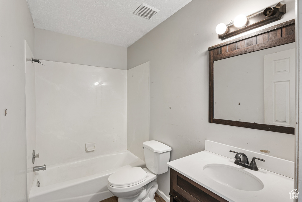 Bathroom with toilet, vanity, a textured ceiling, and  shower combination