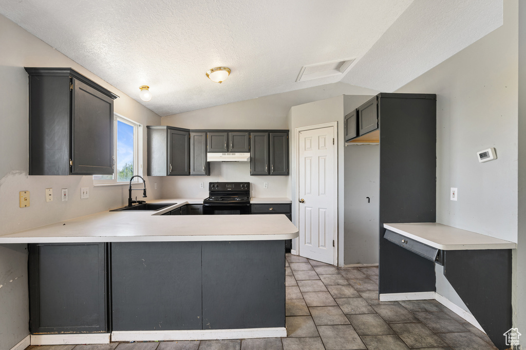 Kitchen featuring black range, a sink, vaulted ceiling, a peninsula, and light countertops