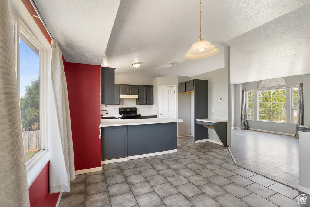 Kitchen featuring a sink, black stove, under cabinet range hood, baseboards, and a peninsula