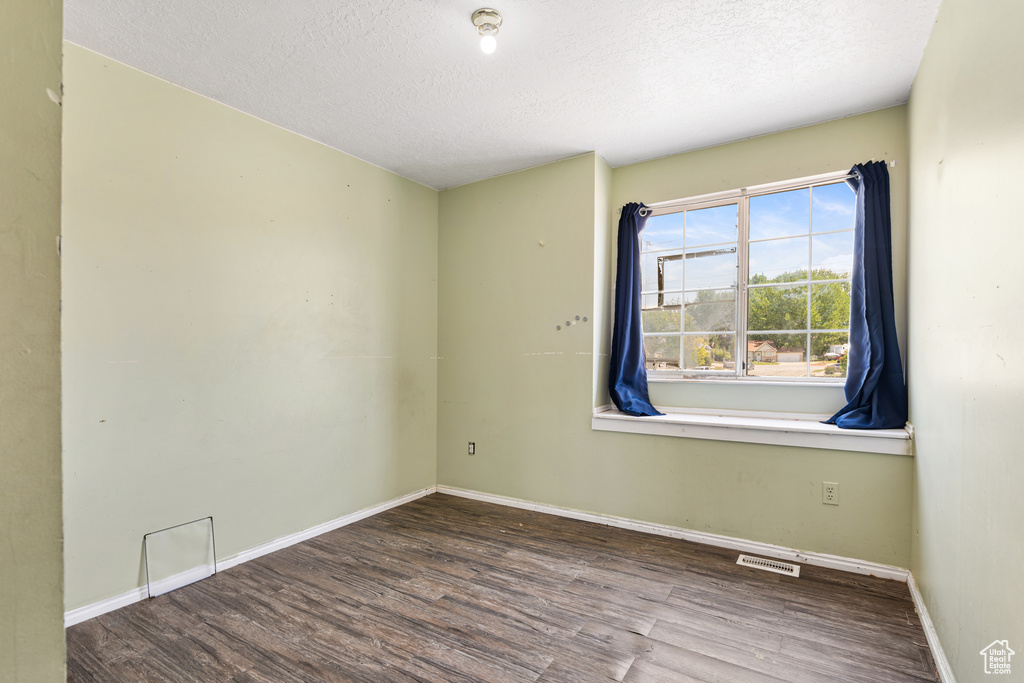 Spare room featuring wood finished floors, a textured ceiling, and baseboards