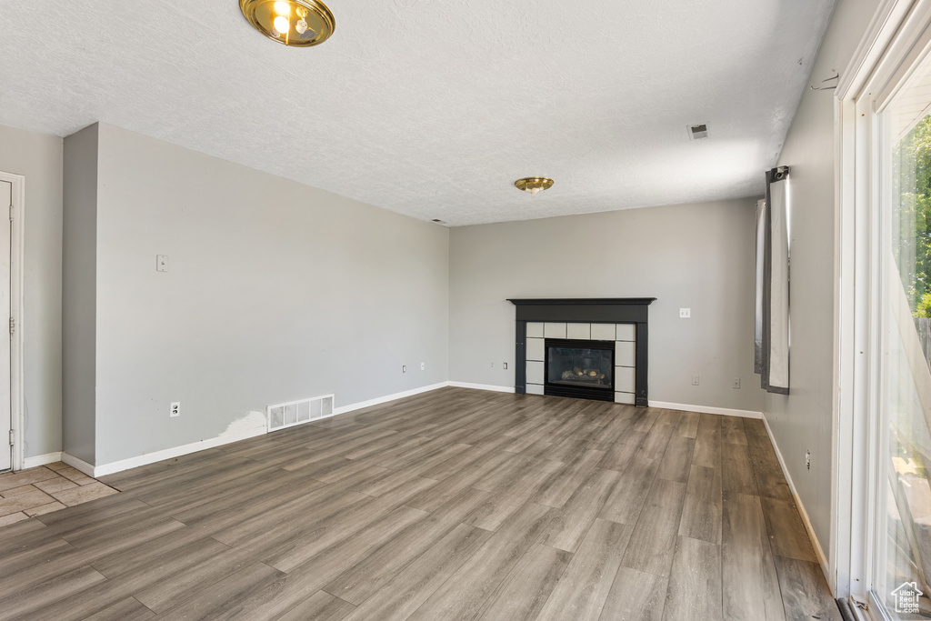 Unfurnished living room with wood finished floors, a fireplace, baseboards, and a textured ceiling
